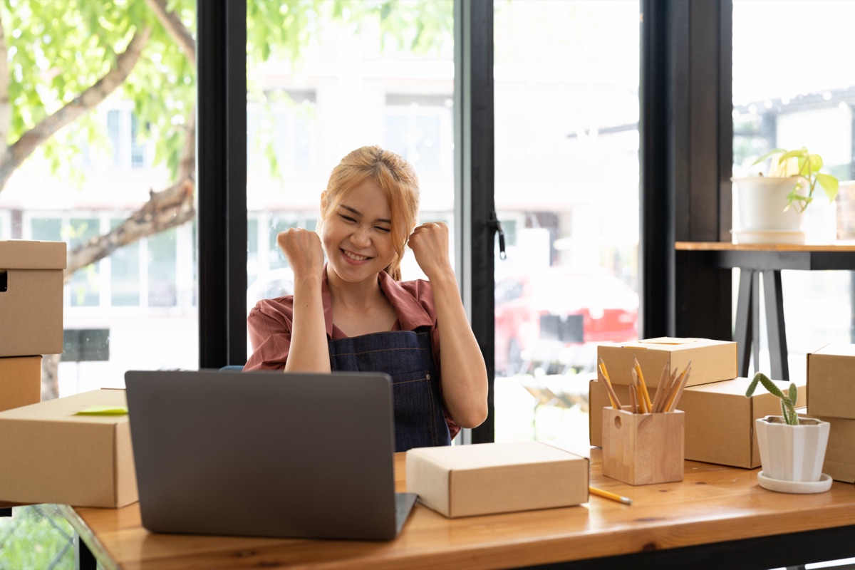 Cheerful small business owner celebrating success at her wooden desk