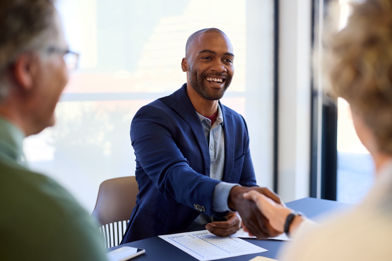 Smiling funding advisor shaking hands with a small business owner across a desk in a bright office